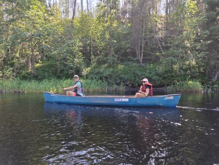 Zwei Personen paddeln in einem blauen Kanu auf einem ruhigen Gewässer, umgeben von üppigem Grün und Bäumen.