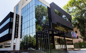 Das moderne Gabrielle International Hotel mit großen Glasfenstern spiegelt die umliegenden Bäume und den blauen Himmel wider.