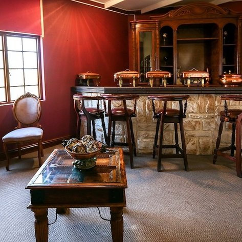 Ein eleganter Barbereich mit Holzstühlen und einem stilvollen Tisch, umgeben von warmen, roten Wänden und natürlichem Licht.