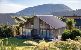 Ein modernes Ferienhaus mit großen Fenstern, umgeben von üppigem Grün und Blick auf sanfte Hügel im Hintergrund.