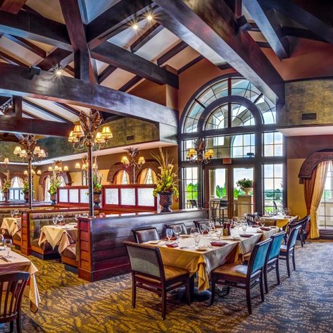 Ein elegantes Restaurant mit Holzbalkendecke, stilvollen Lampen und gedeckten Tischen, die auf einladende Fenster blicken.