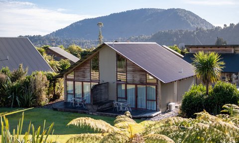 Ein modernes Ferienhaus mit großen Fenstern, umgeben von üppigem Grün und Blick auf sanfte Hügel im Hintergrund.