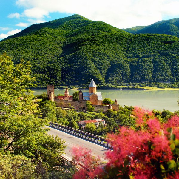 Eine malerische Landschaft mit einem historischen Kloster, umgeben von üppigen grünen Bergen und einem ruhigen See.