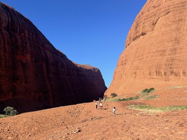 Breiter roter Canyon mit majestätischen Felswänden, wo Menschen auf dem trockenen Boden wandern und den blauen Himmel betrachten.