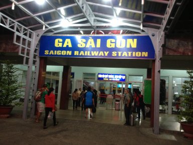 Der Eingangsbereich des Bahnhofs Saigon ist beleuchtet, mit Reisenden, die ihre Koffer tragen und auf Züge warten.