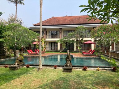 Ein ruhiger Hotelgarten mit einem Pool, umgeben von üppigem Grün und roten Liegen unter Sonnenschirmen.