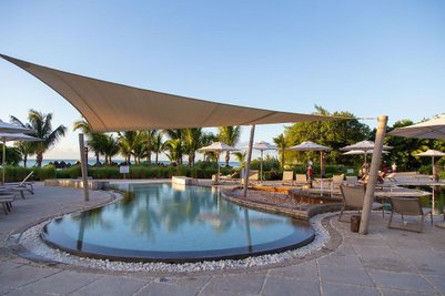 Ein eleganter Poolbereich mit Sonnenschirmen und Liegen, umgeben von Palmen und einer ruhigen Landschaft am Meer.