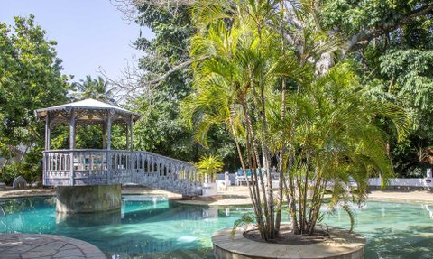 Ein malerischer Pool mit einer Holzbrücke und üppigem Grün umgibt die entspannende Atmosphäre des Resorts.