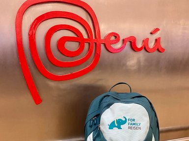 Ein grüner Rucksack mit einem Elefantenlogo steht vor einem roten Peru-Schild in einem modernen Innenraum.