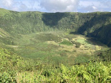 Eine weite, grüne Senke umgeben von steilen Hängen, die mit üppiger Vegetation bedeckt sind, unter einem klaren Himmel.