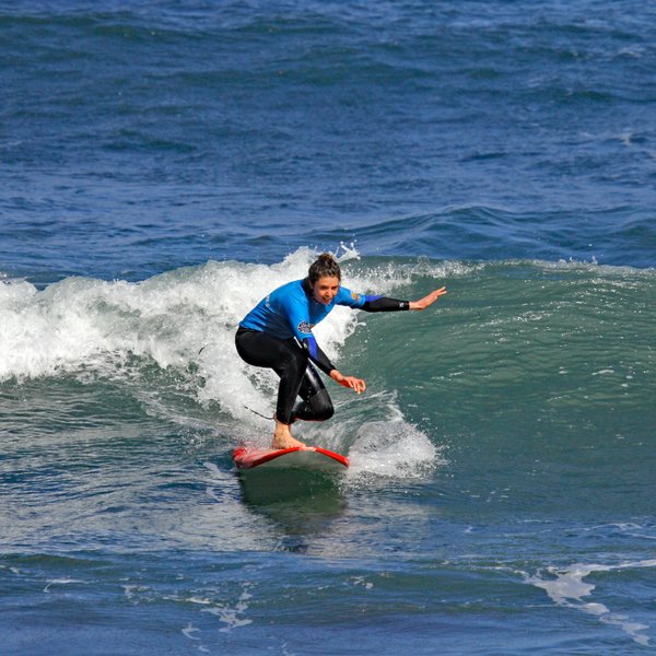 Eine Surferin in einem blauen Neoprenanzug reitet auf einer Welle und zeigt Geschicklichkeit und Balance.