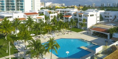 Ein weitläufiger Pool umgeben von Palmen und modernen weißen Gebäuden, ideal für einen entspannten Urlaub in Mexiko.