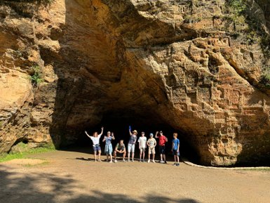 Eine Gruppe von sieben Personen posiert fröhlich vor einer beeindruckenden Felswand im Gauja-Nationalpark.