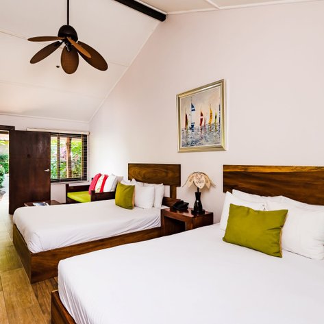 Ein helles Zimmer mit zwei Betten, einem großen Fenster und einem Blick auf einen üppigen Garten im Hintergrund.