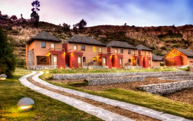 Die malerische Lodge mit strohgedeckten Dächern liegt in einer sanften Hügellandschaft, umgeben von üppigem Grün.