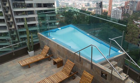Ein moderner Jacuzzi auf einer Dachterrasse mit Blick auf die Stadt Medellín, umgeben von eleganten Liegen und Pflanzen.