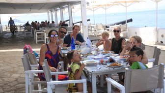 Eine Gruppe von Menschen genießt ein gemeinsames Abendessen am Meer, umgeben von Sonnenschirmen und einem entspannten Ambiente.