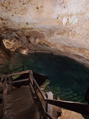 Eine beeindruckende Höhle mit glasklarem Wasser, umgeben von steilen Felswänden und schimmernden Stalaktiten.