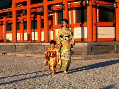 Eine Frau in einem eleganten Kimono und ein kleines Mädchen in einem bunten Kimono spazieren fröhlich im Heian-Schrein.