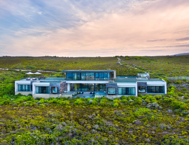 Ein modernes, elegantes Haus mit großen Fenstern steht inmitten einer üppigen, grünen Landschaft unter einem sanften Himmel.