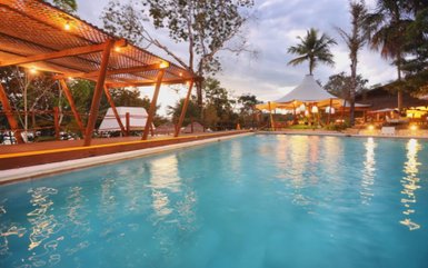 Ein einladender Pool mit klarem Wasser, umgeben von Palmen und einer gemütlichen Terrasse im Hintergrund.