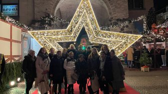 Eine Gruppe von Frauen posiert fröhlich vor einem großen, leuchtenden Weihnachtsstern auf einem festlichen Markt.