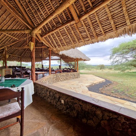 Ein einladendes Restaurant im Tsavo West Nationalpark mit einem Strohdach und Blick auf die grüne Savanne.