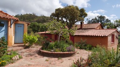 Ein malerischer Garten mit bunten Blumen umgibt rustikale Hütten mit roten Türen und einem blauen Eingang.