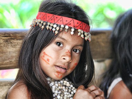 Ein junges Mädchen mit langen, dunklen Haaren und einem bunten Kopfschmuck schaut neugierig in die Kamera.