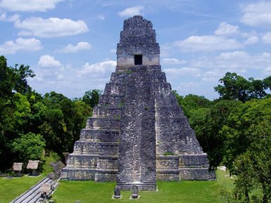 Die beeindruckende Pyramide von Tikal erhebt sich majestätisch über die umliegende grüne Landschaft unter einem strahlend blauen Himmel.