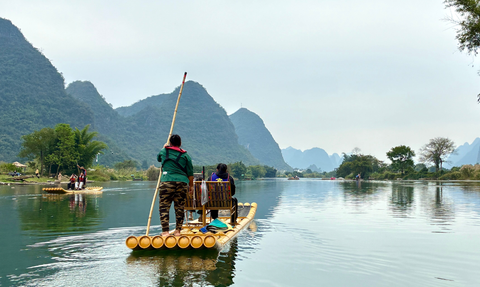 Eine Bambusflossfahrt auf einem ruhigen Fluss, umgeben von majestätischen Bergen und sanften Nebelschwaden.