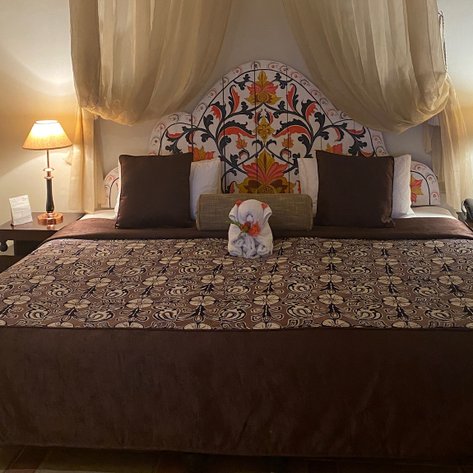 Ein elegantes Hotelzimmer mit einem kunstvoll verzierten Bettkopf und sanften Vorhängen, die eine gemütliche Atmosphäre schaffen.