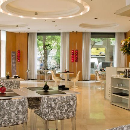 Ein eleganter Innenraum eines Restaurants mit stilvollen Tischen und Stühlen, umgeben von großen Fenstern und Pflanzen.