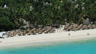Ein atemberaubender Blick auf einen weißen Sandstrand, gesäumt von Palmen und traditionellen Strohhütten.