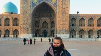 Eine Frau steht lächelnd vor der beeindruckenden Architektur des Registan in Samarkand, umgeben von Besuchern.