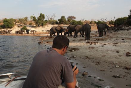 Botswana Familienreise - Botswana for family individuell - Chobe Nationalpark - Mann fotografiert Elefantenherde vom Boot aus