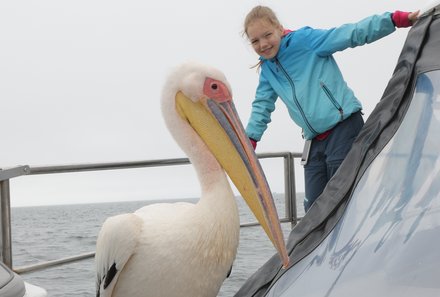 Namibia mit Kindern - Namibia Rundreise mit Kindern - Bootsfahrt zu Walvis Bay - Pelikan mit Mädchen auf Boot