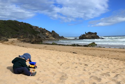 Garden Route mit Kindern individuell - Kind sitzt im Sand am Strand von Knysna