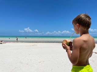 Mexiko Familienreise - Kind am Strand mit einer Kokosnuss