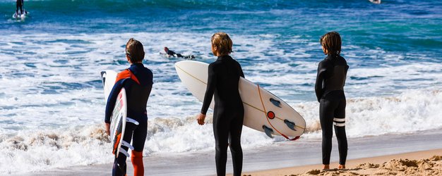 Algarve for family - Familienreise Algarve mit Kindern - Kinder stehen mit Surfbrettern am Wasser